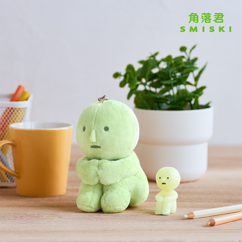 SMISKI knee-hugging plush charm on a desk; small figure and props shown for display only
